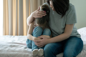 mother comforting daughter while sitting on a bed