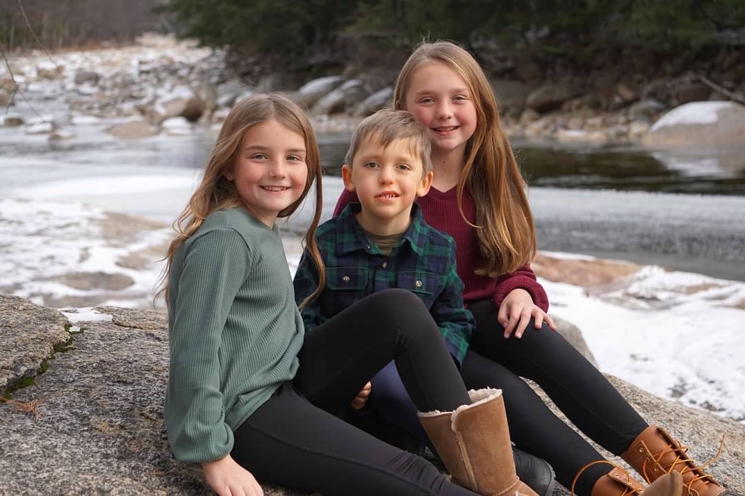 Colin, who was born with infantile scoliosis, hangs out with his sisters on some boulders next to a stream.