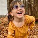 Harper, who was born with a brachial plexus injury, laughs in a pair of round sunglasses.