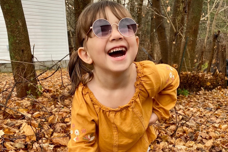 Harper, who was born with a brachial plexus injury, laughs in a pair of round sunglasses.
