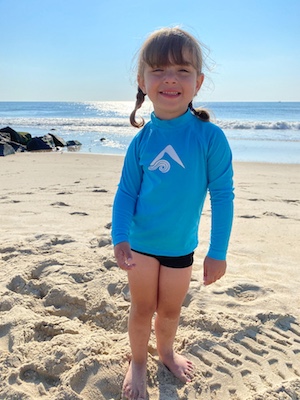 Harper, who was born with brachial plexus injury, stands on the beach. Her right shoulder is visibly lower than her left (uninjured) shoulder.