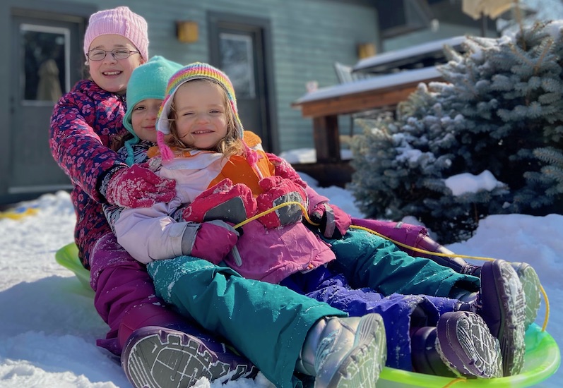 Caroline, who was treated for PVS, sits on a sled with her two sisters in the snow. 