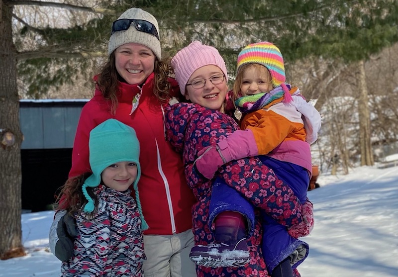 Caroline, who was treated for pulmonary vein stenosis, poses outside in the snow with her mom and two older sisters. 