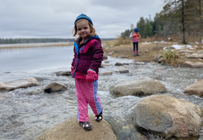 Caroline, who was treated for pulmonary vein stenosis, standing on rocks at a lake