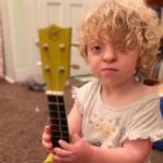 Maisie, who has Apert syndrome, holds a guitar