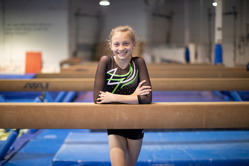 Ashley, who was born with symbrachydactyly, stands smiling next to a balance beam. 