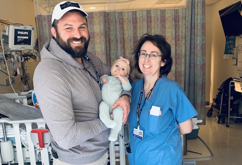 A dad and baby pose with their nurse in the cardiac intensive care unit. 