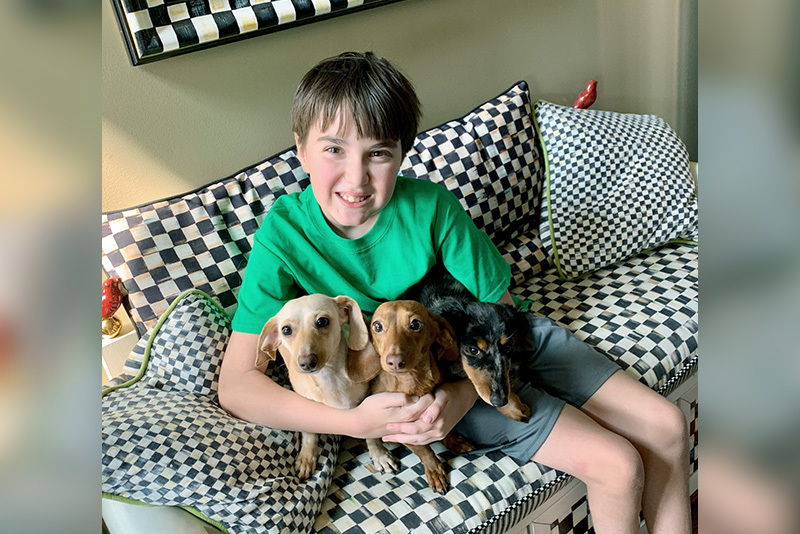 Cooper, who has cerebral palsy, cuddles on a black and white couch with three small dogs