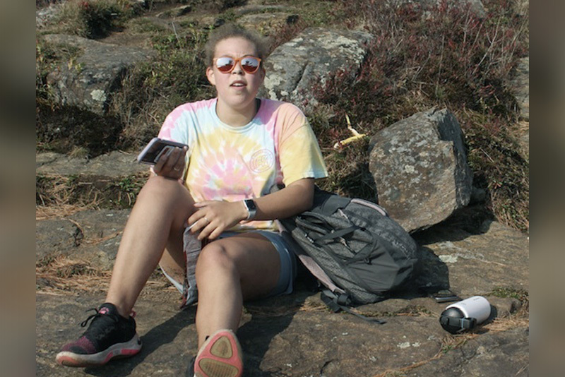 emily, who has graves' disease, sits on a beach after a hike.