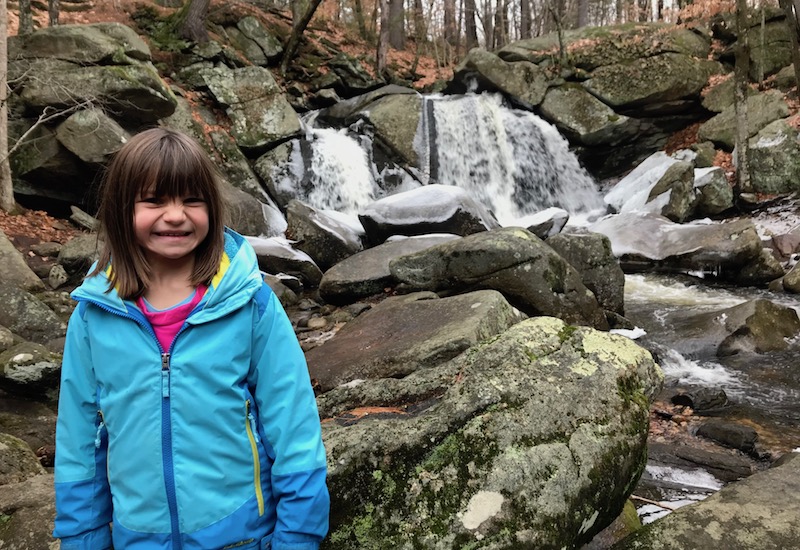 Anna, who has Shwachman-Diamond syndrome, stands in front of a waterfall.
