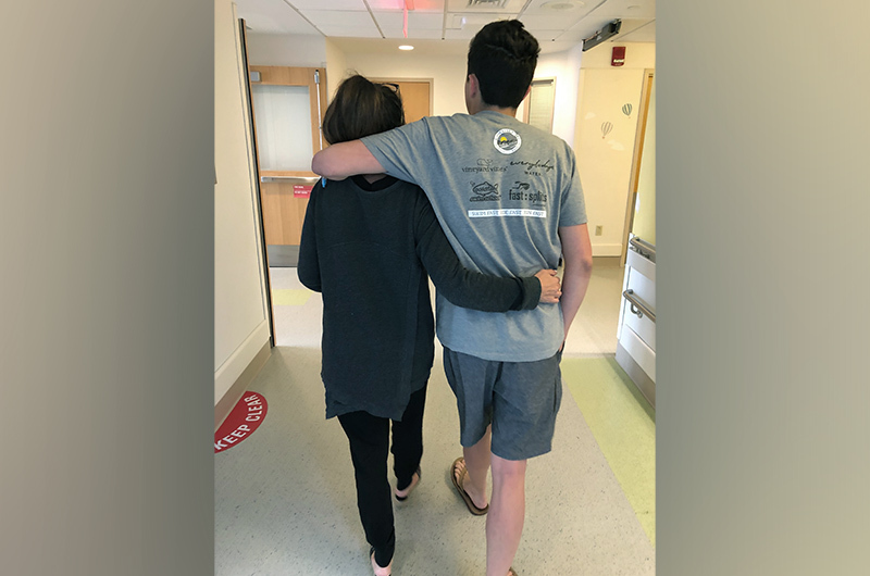 Dylan, who had a TBI, walks down a hospital hallway with his mom. 