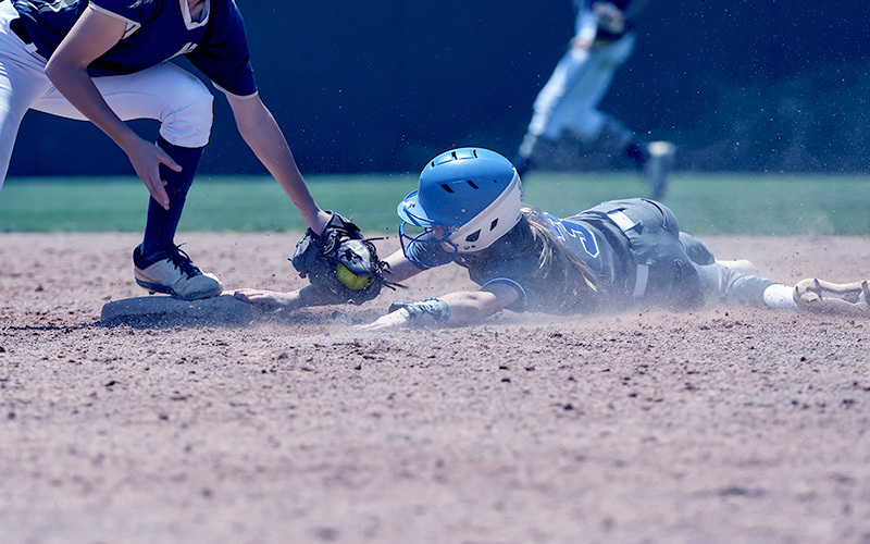 An athlete slides into home plate while another player tags her out.