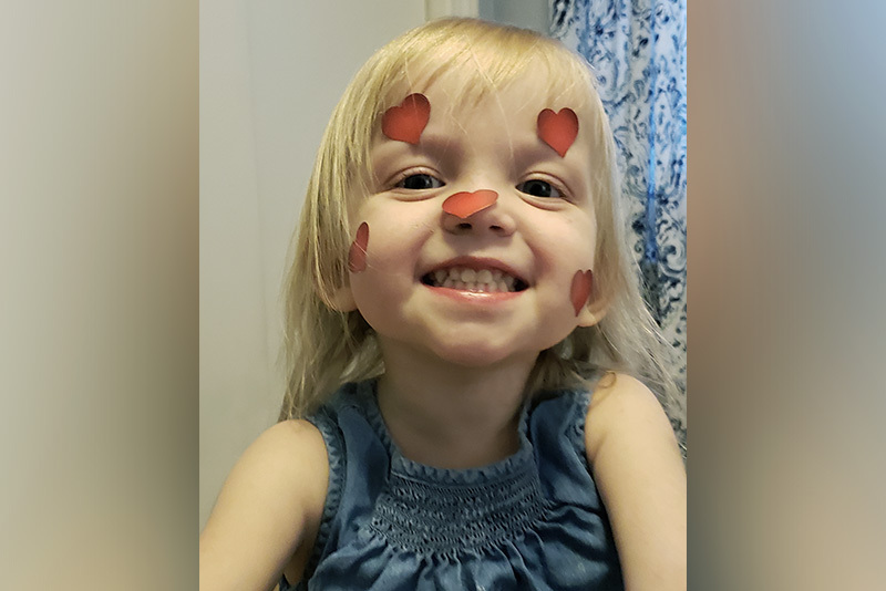 sarah, who has biliary atresia, smiles at the camera with heart stickers on her face