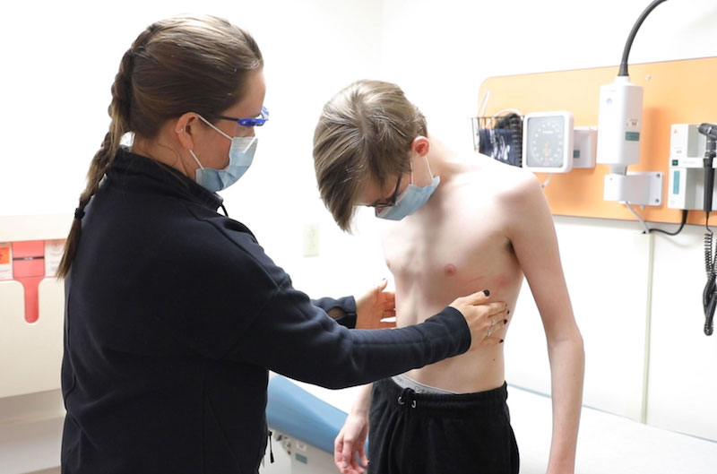 A nurse practitioner assesses the chest of a young man undergoing vacuum bell therapy for mild pectus excavatum.