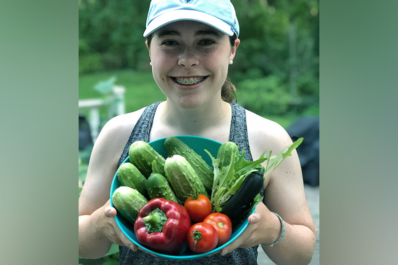 abby holds a bowl full of fresh vegetables from her garden