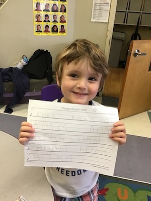 Adam, who was able to attend school in person during COVID-19, holds up a sheet where he has practiced writing his name. 