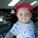 a photo of baby miles with an NG tube in his nose. he is wearing a red hat