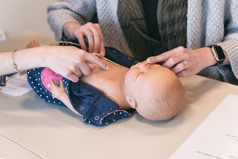 a photo of a baby mannequin. a nurse is showing a mom how to place an NG tube in the doll.