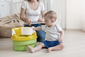 a toddler sits by a training potty with his mom