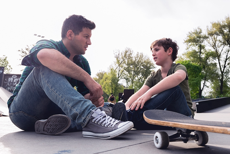 In a chat about bullying, a dad sits to the right of a child, who is also seated outdoors.