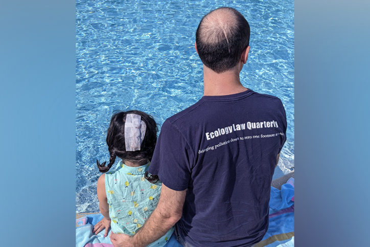 charlotte and her dad sit at a pool with their backs to the camera, showing off their scars