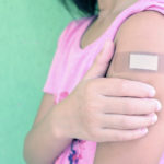 a child holds her arm, which has a bandaid, after getting her covid vaccine