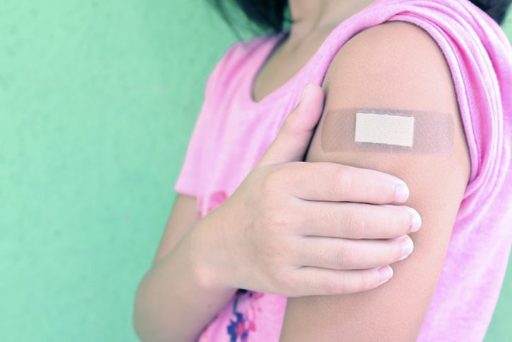 a child holds her arm, which has a bandaid, after getting her covid vaccine