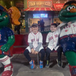 kyle and tyler pose with wally the green monster mascot. they are all wearing red sox shirts