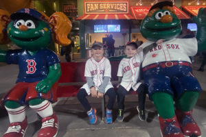 kyle and tyler pose with wally the green monster mascot. they are all wearing red sox shirts