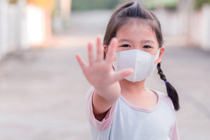 A young, masked girls holds her hand up to indicate "stop."