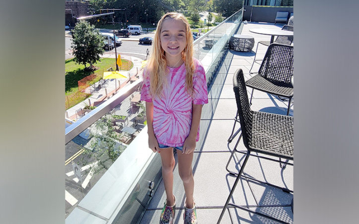 Echo stands on a roof deck smiling at the camera after treatment for midaortic syndrome.