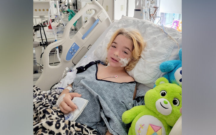 Echo lies in a hospital bed with her Care Bear toys after surgery for midaortic syndrome