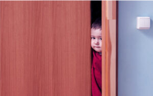 A young child peeking through a door way.