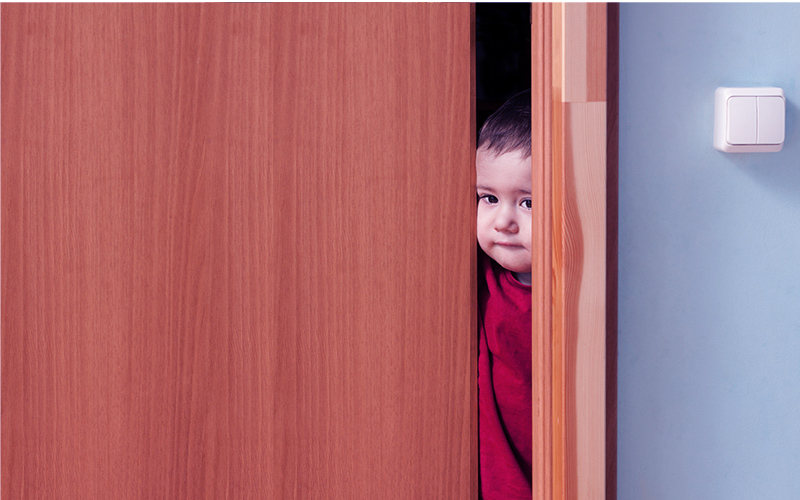A young child peeking through a door way.