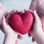 A clay heart held lovingly in a child's hands, which are cupped by a mother's hands.