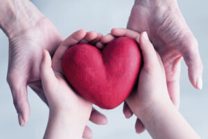 A clay heart held lovingly in a child's hands, which are cupped by a mother's hands.