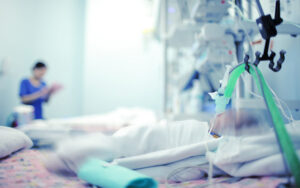 Critically ill child in ICU, with care provider in the background.