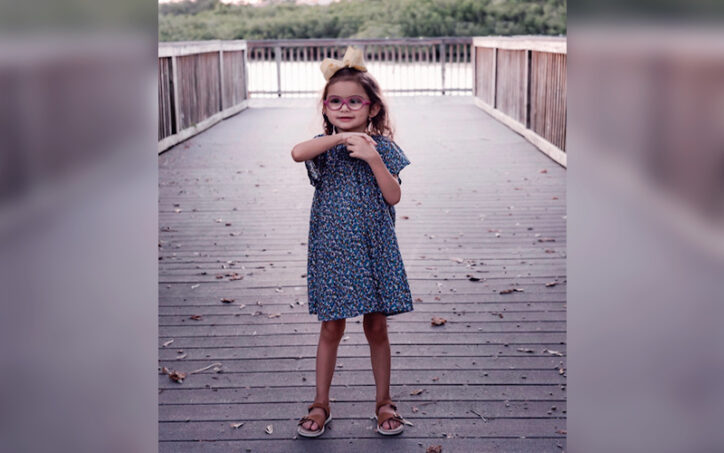 A young girl wearing a dress and glasses wringing her hands.