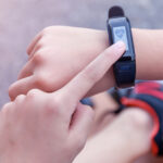 The photo is a closeup of a child's left index finger touching the screen of a wearable device on the right wrist.