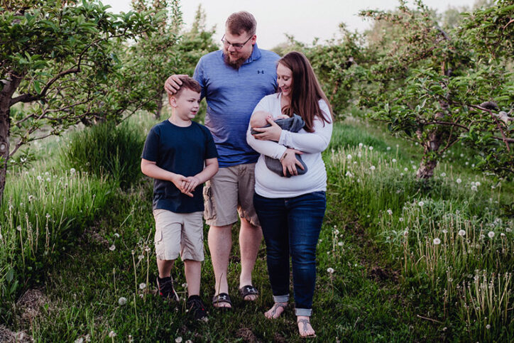 The Allis family walks through an apple orchard, subtly posing for a professional photograph.