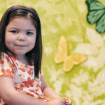 Kira, who had a kidney transplant, smiles next to a wall decorated with butterflies