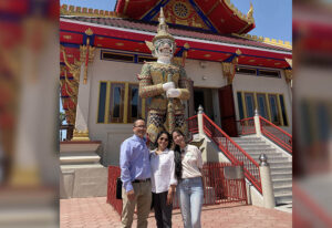 Mother, father, and daughter stand smiling in front of an ornate building.