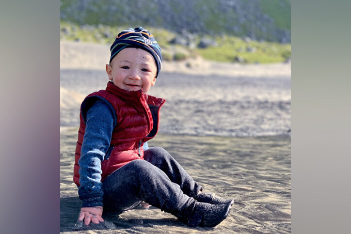 Then 18 months old, Levi smiles for the camera as he sits on a beach in the Lofoten Islands, Norway, 