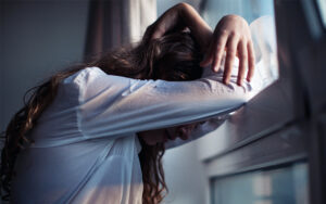 An adolescent girl doubled over in despair, to illustrate concept of suicidality.