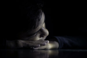 An adolescent boy dark-lit, looking toward a small mount of light