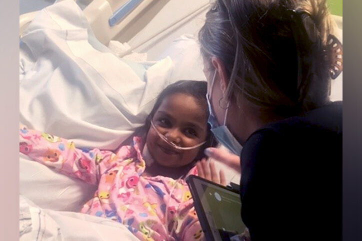 Kyleigh, in her hospital bed, smiles at a Boston Children's Child Life Services employee.