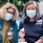 Nurses Marybeth Bentson and Theresa Pak sit together holding a model kidney.