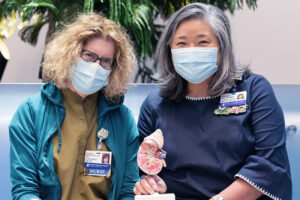 Nurses Marybeth Bentson and Theresa Pak sit together holding a model kidney.