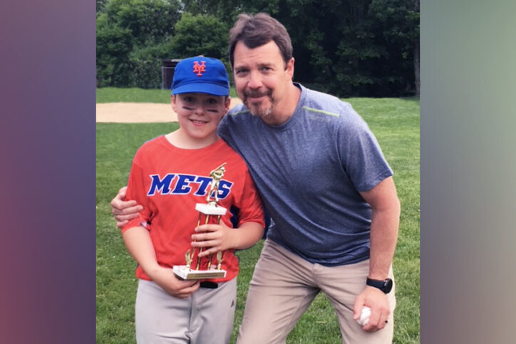 Quinn, who had flexible flatfoot, in a baseball uniform holding a trophy with his dad.