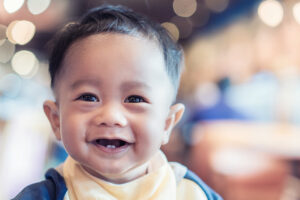 An infant smiles, displaying two lower baby teeth.